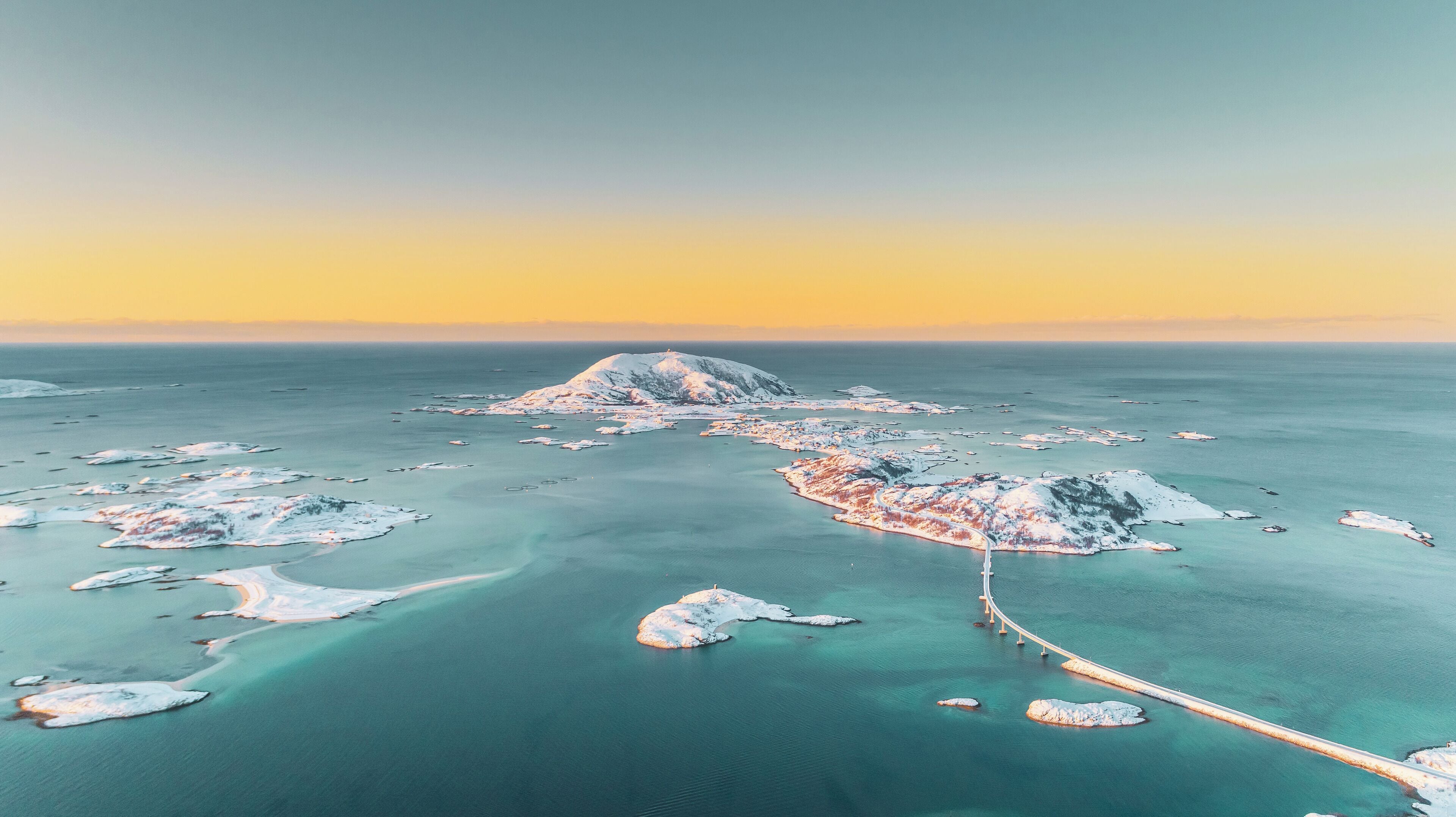 An aerial view of a coastal area with snow-covered islands and a bridge connecting them.