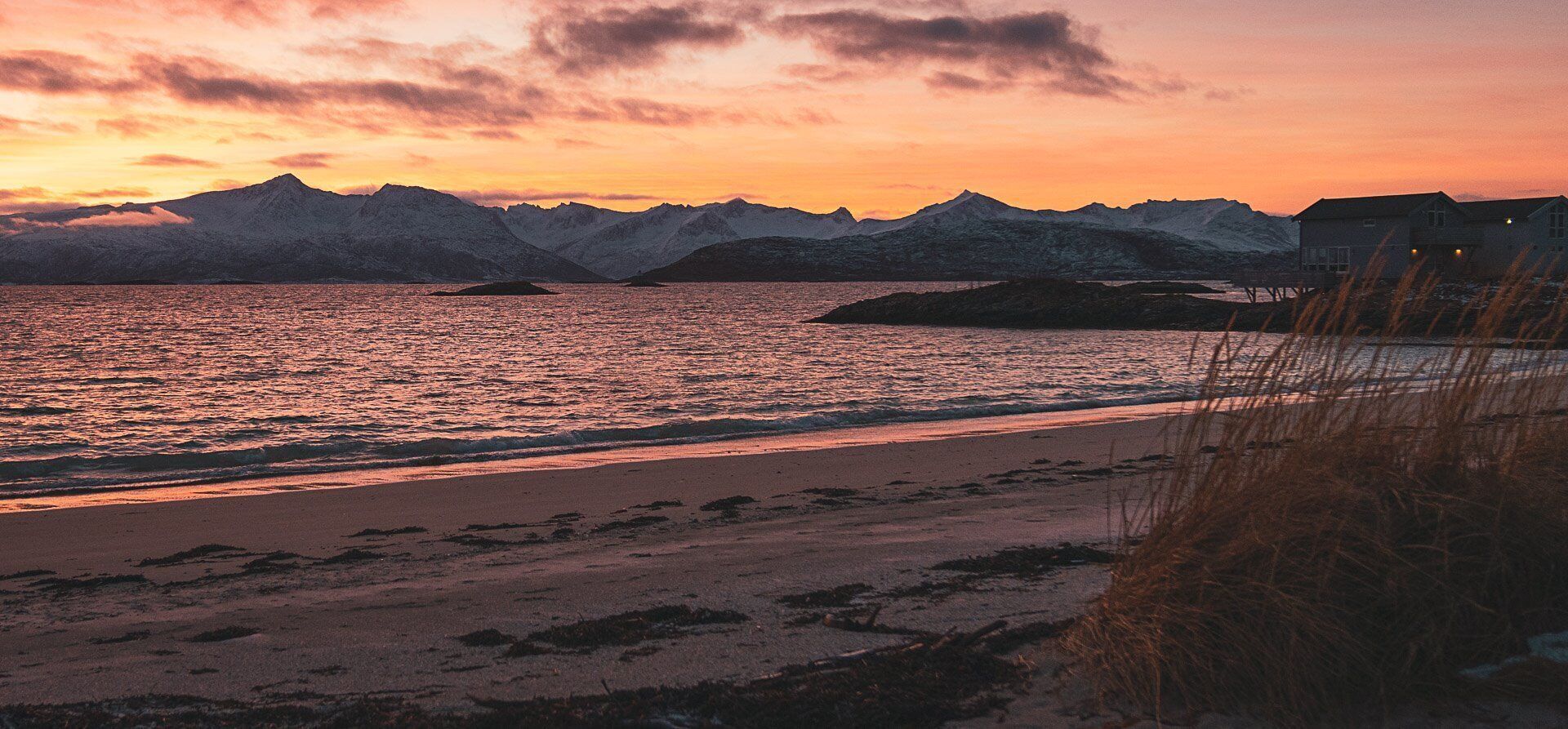 A beach with mountains in the background and a house on stilts to the right.