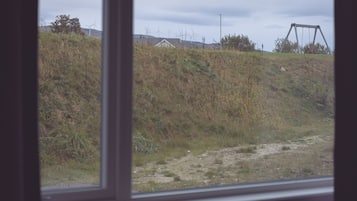 A view through a window of a grassy area with a swing set and wind turbines in the background.