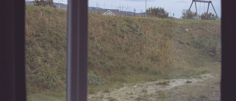 A view through a window of a grassy area with a swing set and wind turbines in the background.