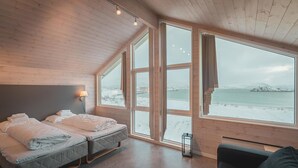 A cozy room with two beds, a window with a snowy landscape view, and a small table with a candle. - Sommarøy Arctic Hotel Tromsø (Tromsø)