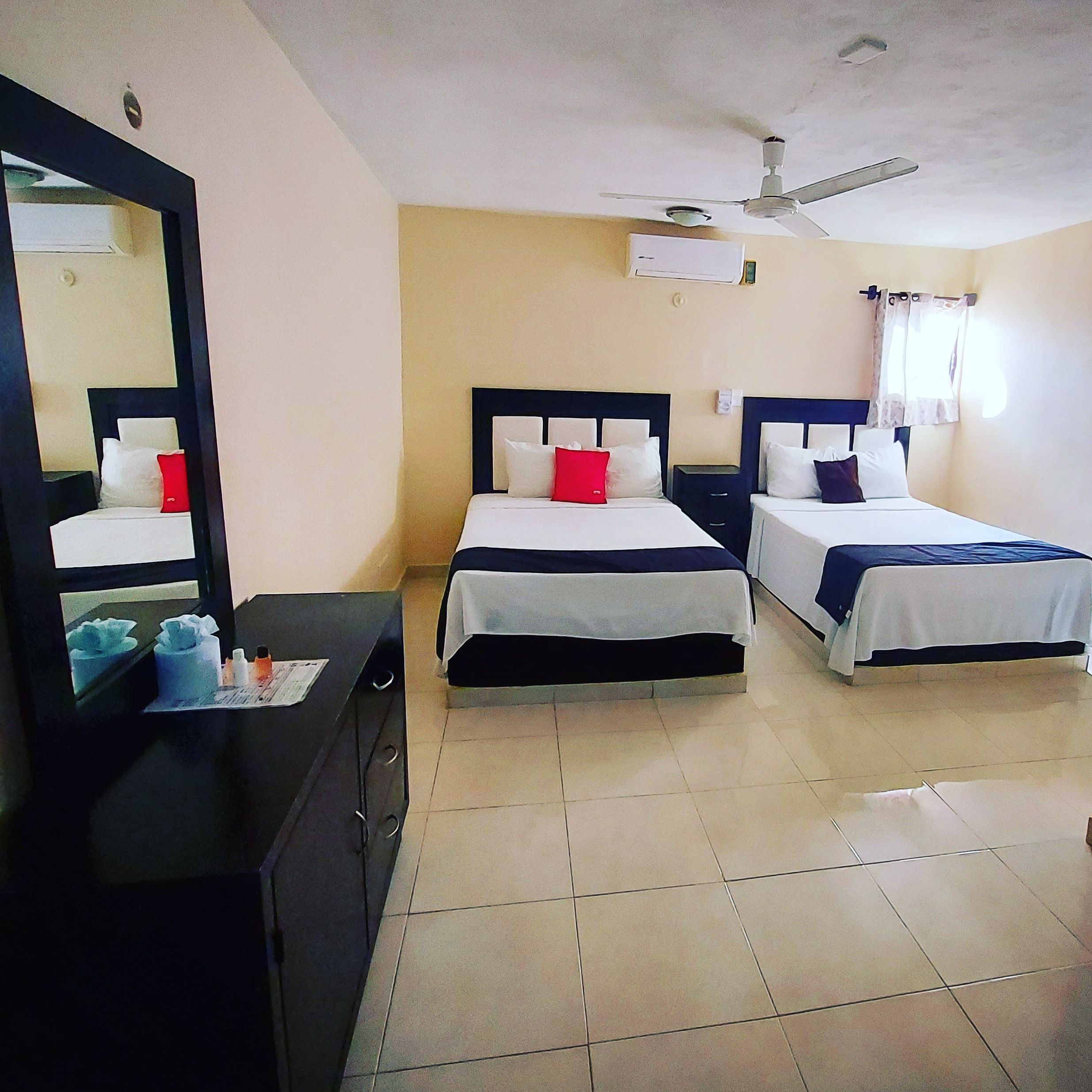 A hotel room with two beds, a mirror, a ceiling fan, and an air conditioning unit.