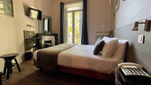 A hotel room with a bed, a desk, a chair, a telephone, and a window with curtains. - Le Strasbourg Hotel (Montpellier)