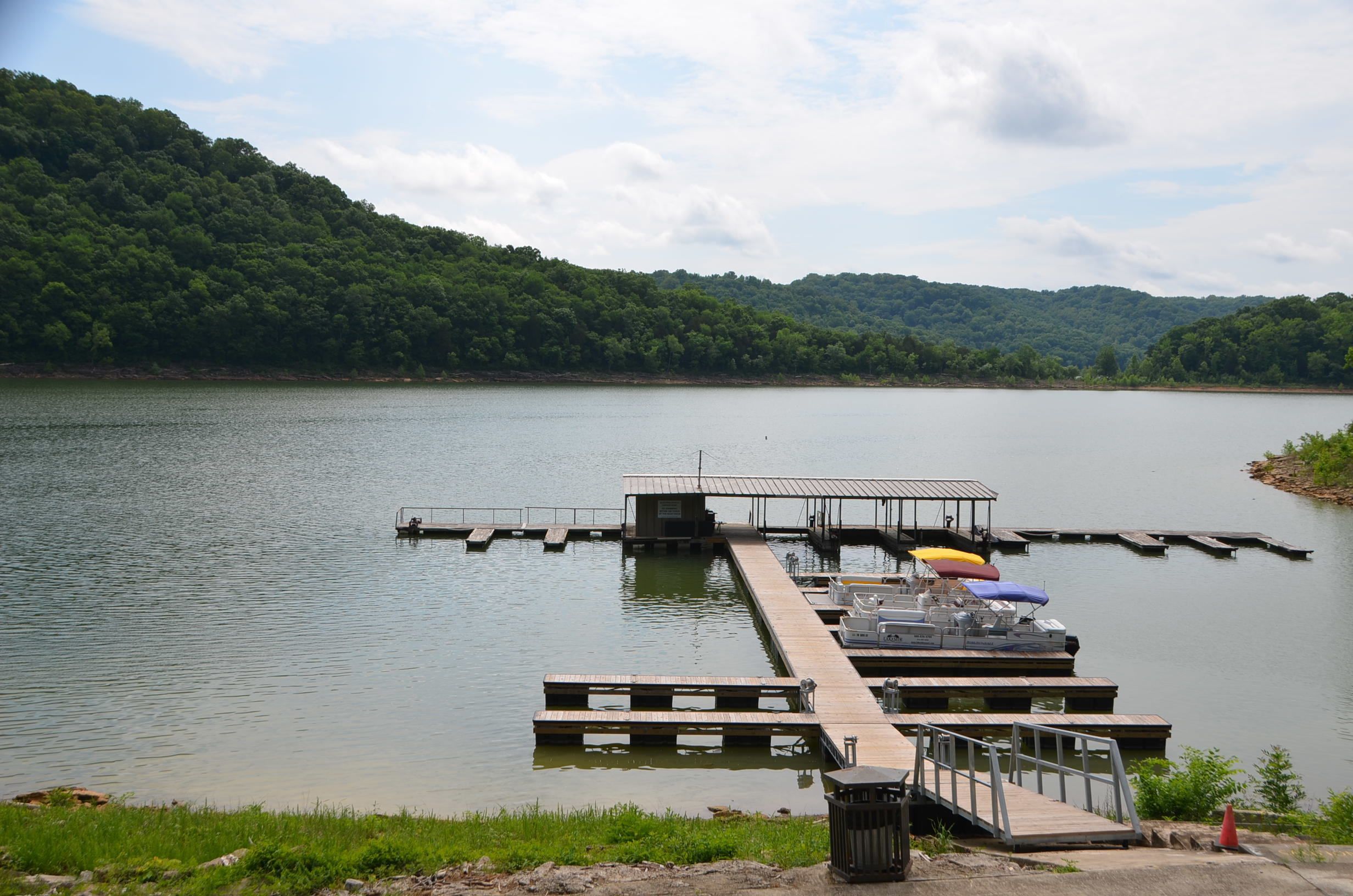 A dock extending into a calm lake with a forested hillside in the background.