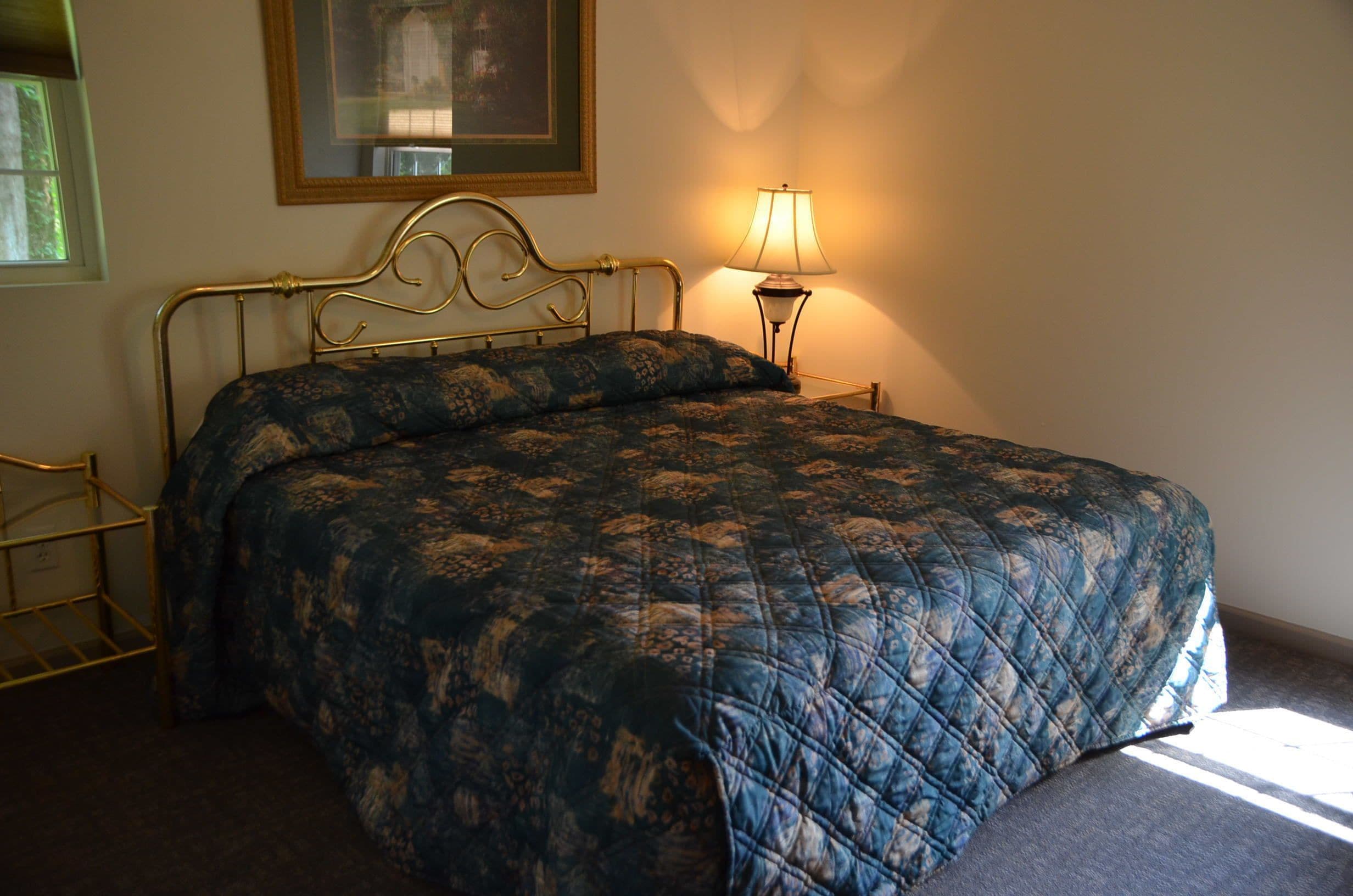 A bed with a quilted headboard, a bedside lamp, and a framed picture on the wall.