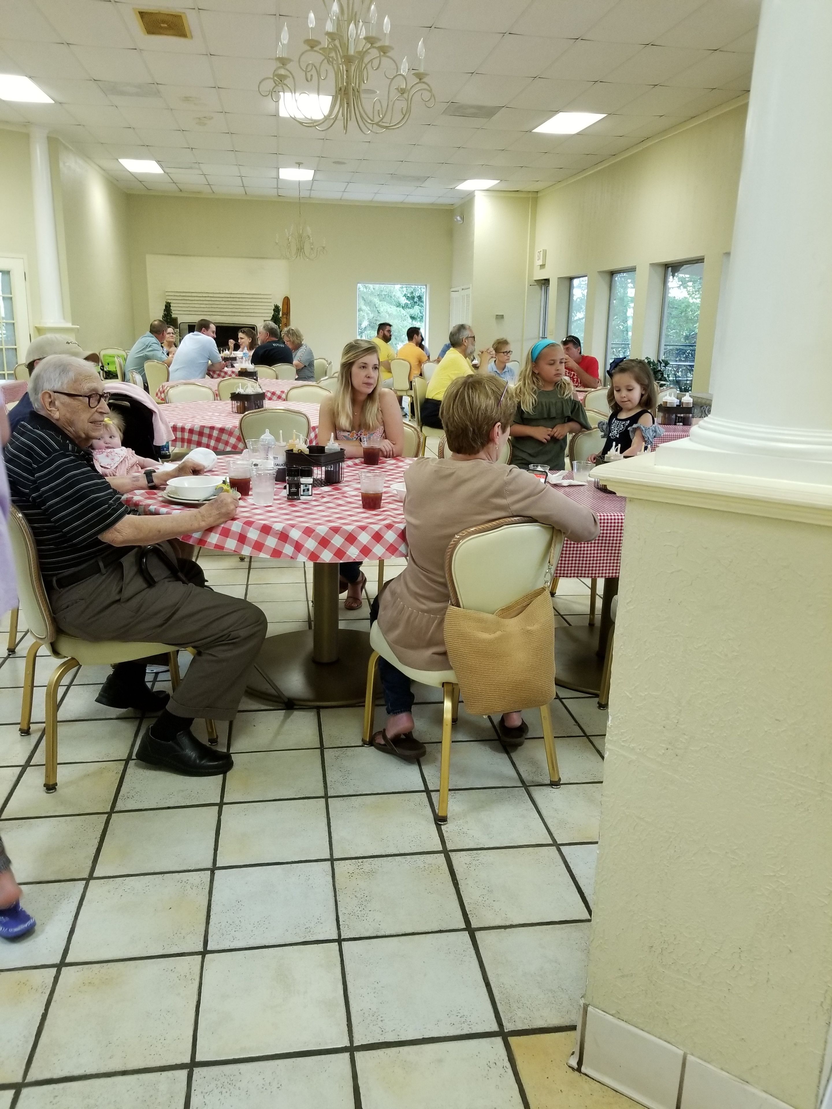 A dining area with checkered tablecloths, people seated at tables, and a chandelier.