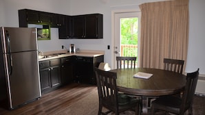 A compact kitchen with dark cabinets, a stainless steel refrigerator, and a wooden dining table with four chairs. - The Retreat at Center Hill Lake (Smithville)