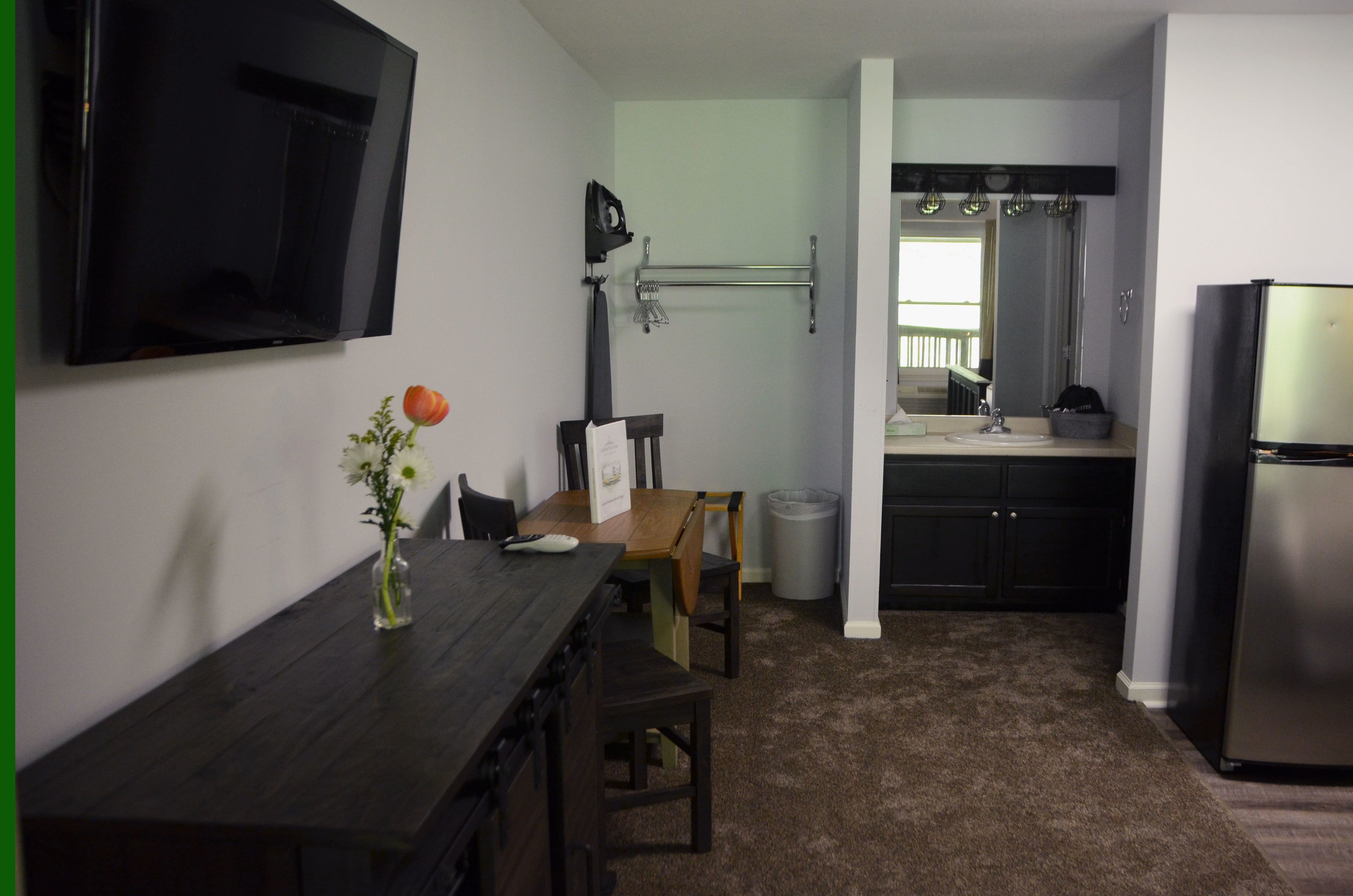 A compact kitchen with a dark wooden table, a vase with a flower, and a TV mounted on the wall.