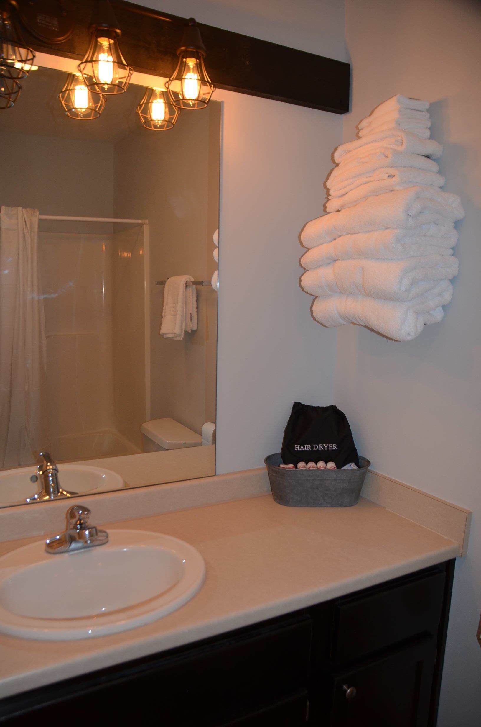 A bathroom with a sink, mirror, towel rack, and a hair dryer basket.
