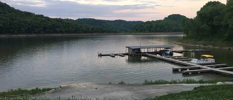 Un muelle a orillas de un lago con un pequeño edificio, rodeado de vegetación y un lago tranquilo.