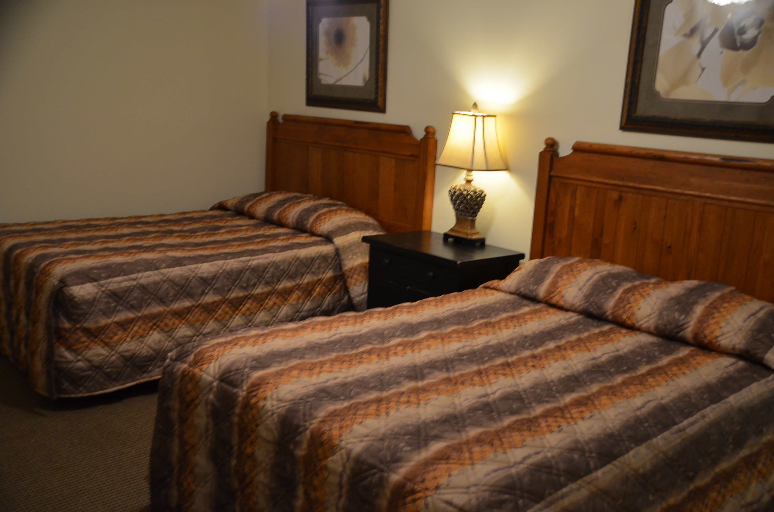 Habitación de hotel con dos camas, una mesita de noche con lámpara y cuadros en las paredes.