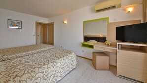 A hotel room with a bed, a desk with a TV, a mirror, and a wall-mounted air conditioner.