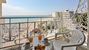 A balcony with a table set for breakfast, overlooking a beach with umbrellas and people.