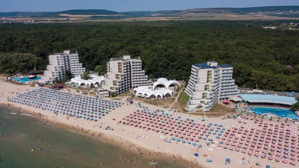 A beach resort with multiple hotel buildings, numerous beach umbrellas, and a large swimming pool.