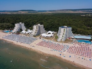 Un complejo turístico en la playa con varios edificios de hotel, numerosas sombrillas y una gran piscina.