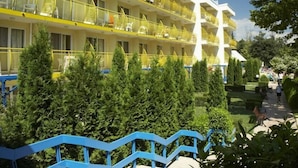 Un hotel a più piani con balconi, una torre centrale bianca e un giardino curato con recinzione blu.