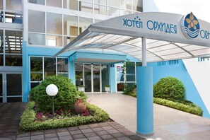 A hotel entrance with a blue and white facade, a covered entrance area, and a sign with Cyrillic script. - Hotel Orchidea Park All Inclusive (Albena)