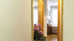 A narrow hallway with a carpeted floor leading to a bedroom. A potted plant with pink flowers is visible on the left. - Iberos Jaén (Jaén)