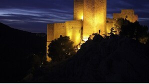 A historic castle with multiple towers, illuminated at night, surrounded by trees and hills. - Iberos Jaén (Jaén)