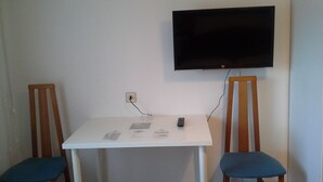 A small room with a white table, two wooden chairs, a flat-screen TV mounted on the wall, and a power outlet on the wall. - Iberos Jaén (Jaén)