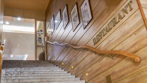 A wooden staircase with a handrail leading to a wall with framed artwork and the word "RESTAURANT" visible. - Hotel Sandy Beach (Albena)