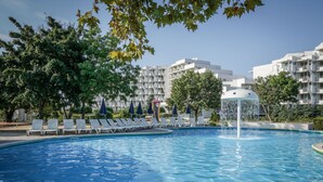 A swimming pool with lounge chairs and a water fountain, surrounded by trees and modern buildings. - Hotel Sandy Beach (Albena)