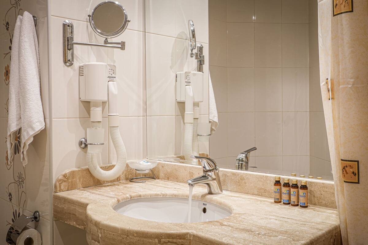 A bathroom with a sink, mirror, towel rack, and toiletries.