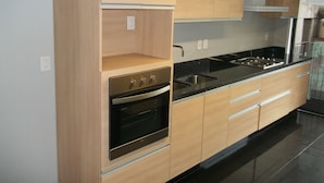 A modern kitchen with light wood cabinets, a black countertop, stainless steel appliances, and a built-in oven. - Polanco by O (Mexico City)