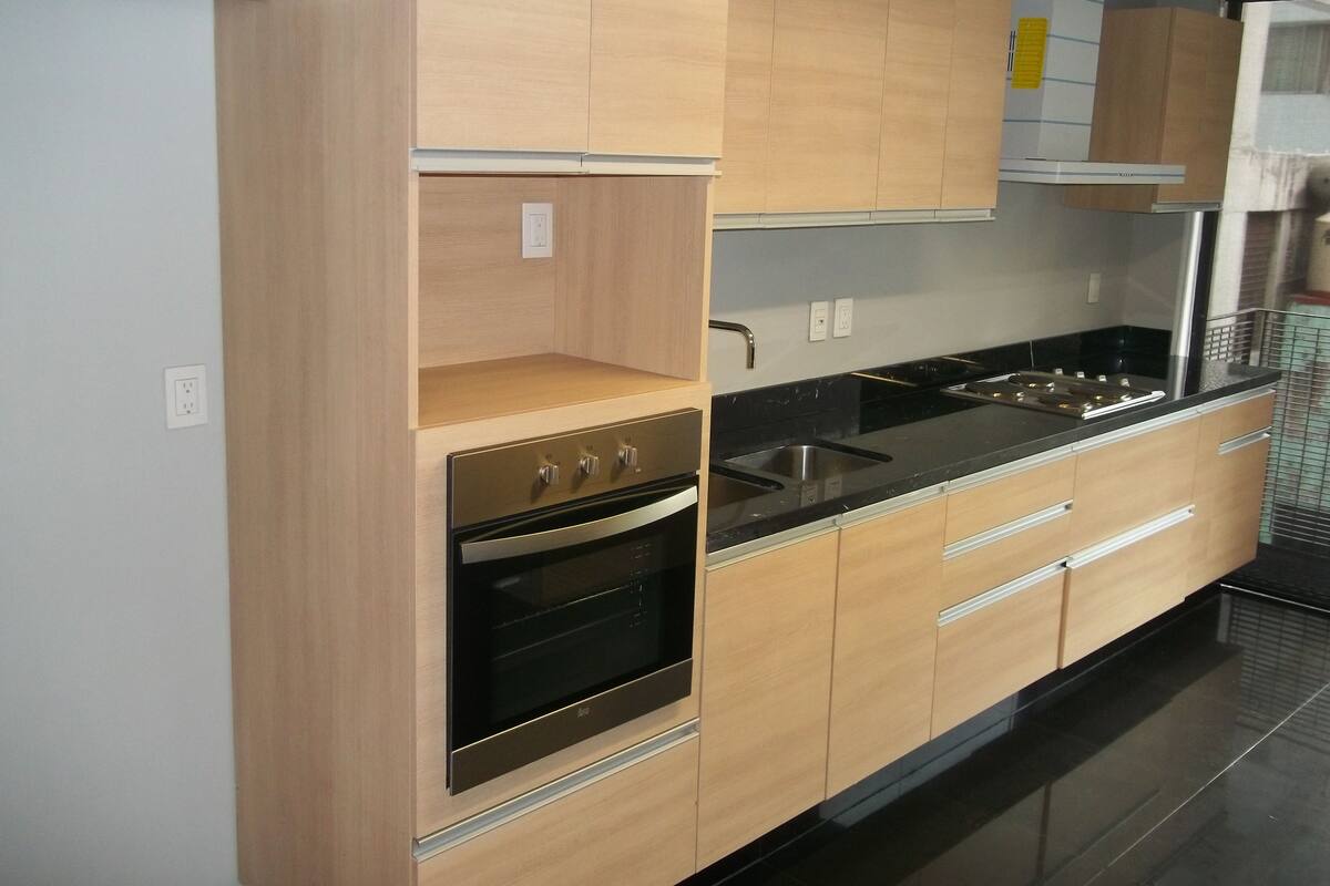A modern kitchen with light wood cabinets, a black countertop, stainless steel appliances, and a built-in oven.