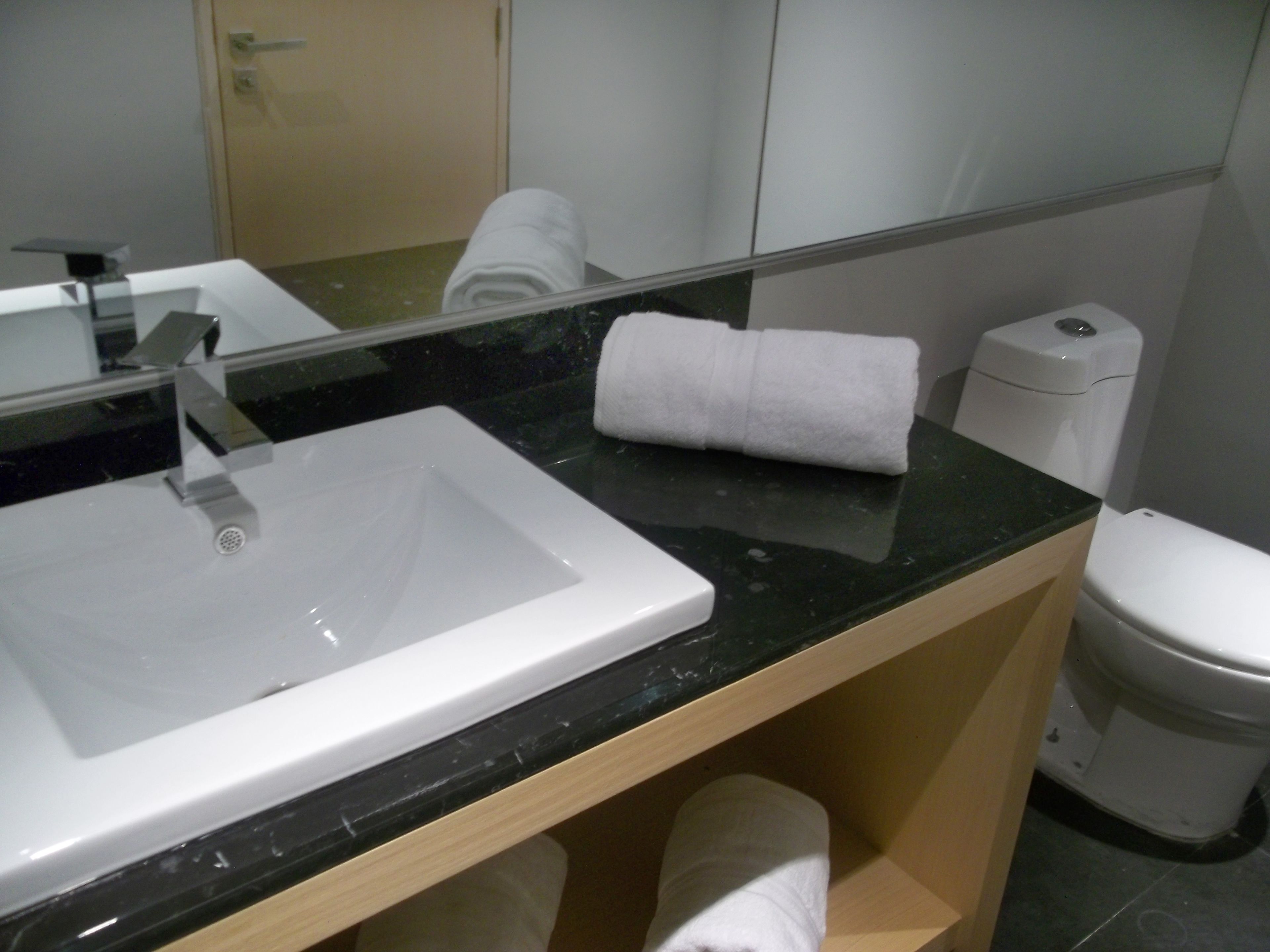 A bathroom with a white sink, a mirror, a toilet, and a towel on the counter.
