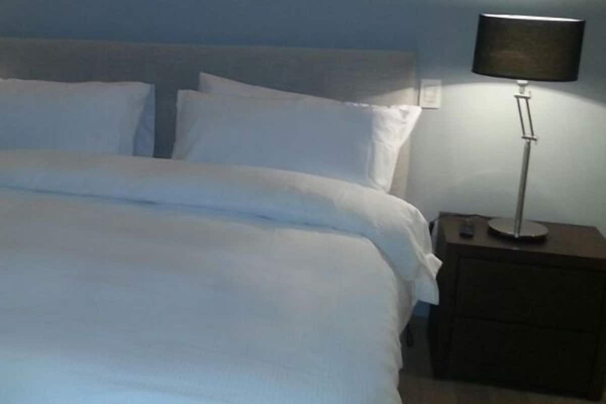 A neatly made bed with white bedding, two bedside tables with lamps, and a plain wall in the background.