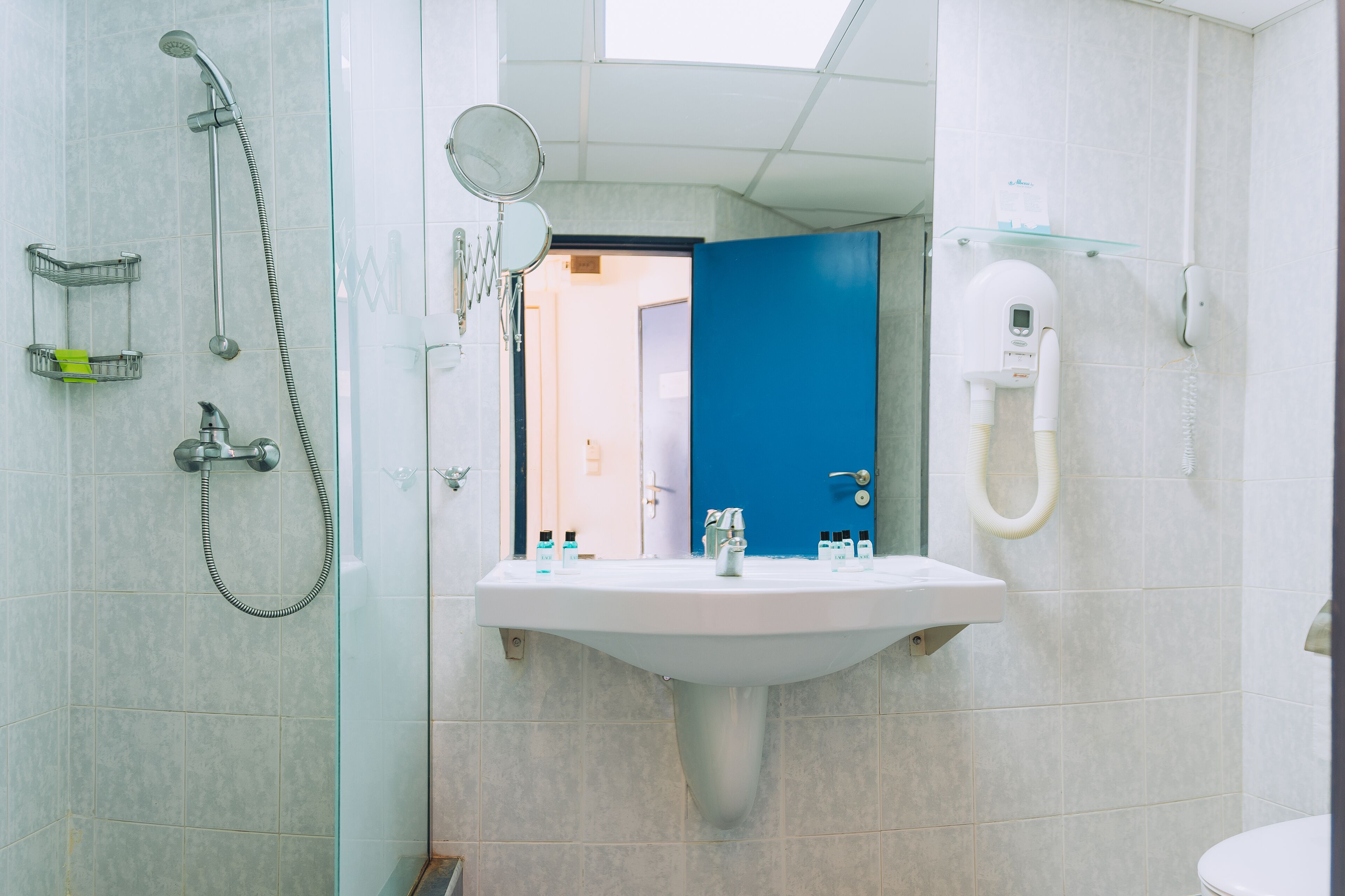 Baño con ducha, lavamanos y espejo. Se observa una puerta azul al fondo.