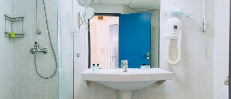 Baño con ducha, lavamanos y espejo. Se observa una puerta azul al fondo.