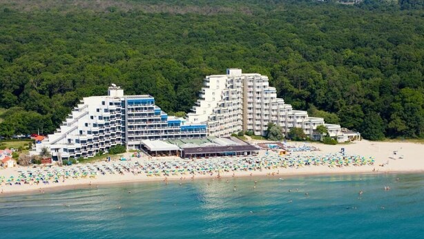 Un hôtel situé en bord de mer, composé de plusieurs bâtiments, avec une plage de sable et une zone boisée en arrière-plan.