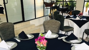 A round table set for a meal with a vase of pink flowers in the center, surrounded by chairs and plates with napkins. - Hotel Marina Topolobampo (Topolobampo)