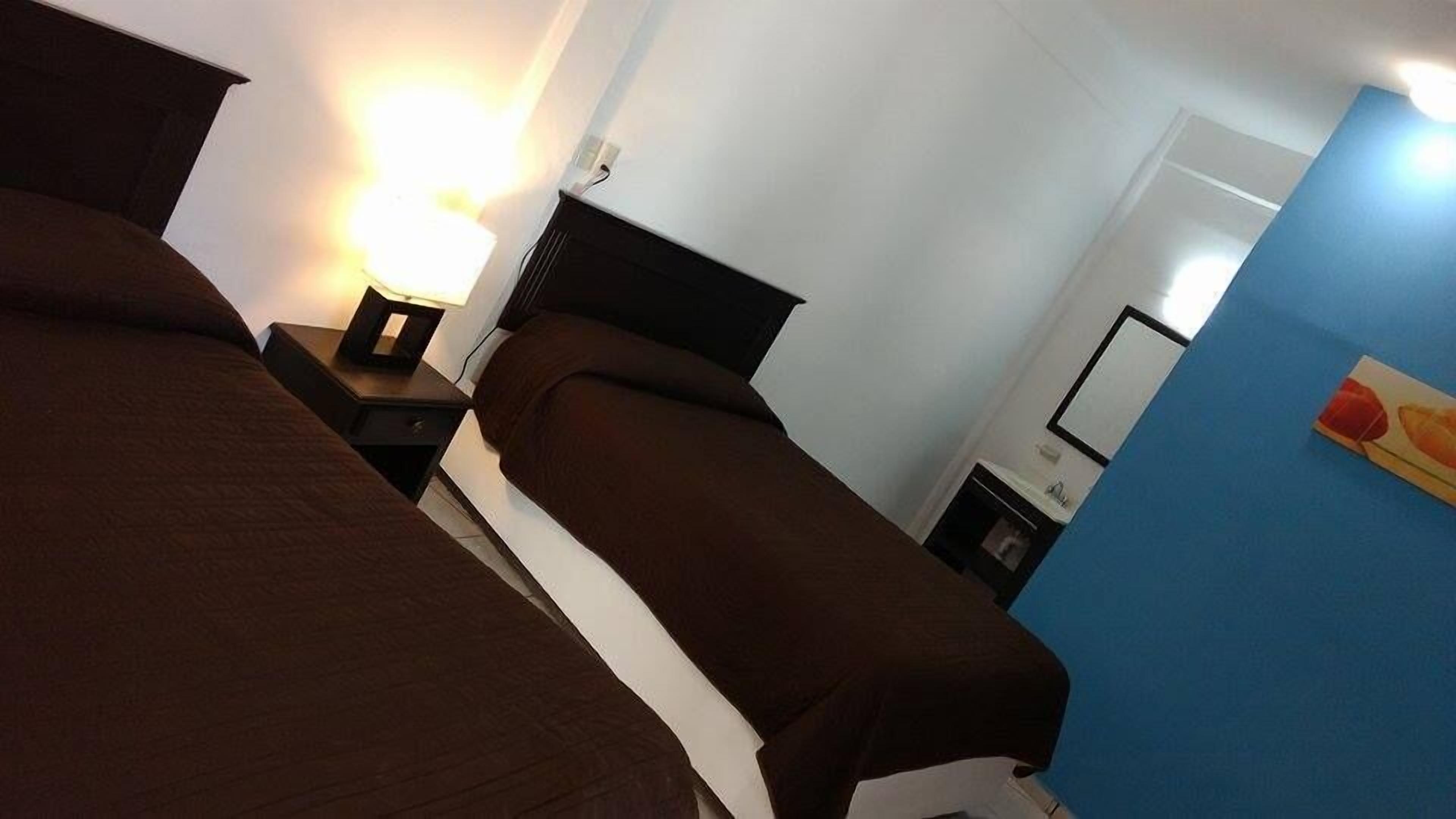 A hotel room with two beds, a nightstand with a lamp, a small table, and a mirror.