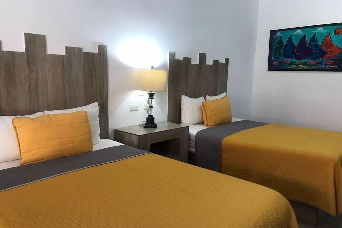 A hotel room with two beds, a nightstand with a lamp, and a painting on the wall.