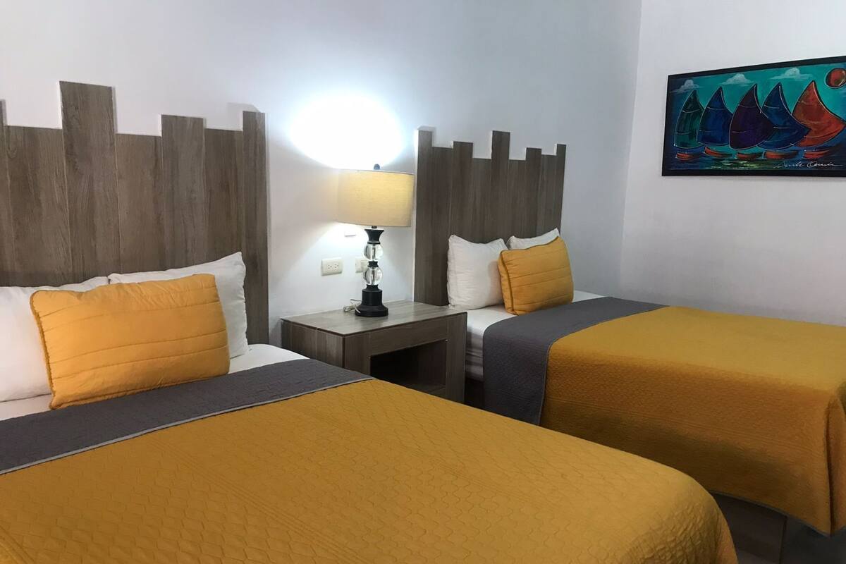 A hotel room with two beds, a nightstand, a lamp, and a painting on the wall.