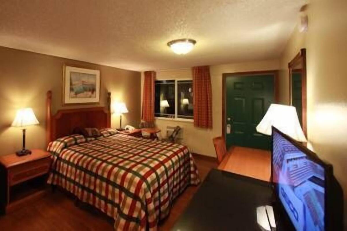 Habitación de hotel con cama, escritorio con computadora, silla, televisor y puerta.
