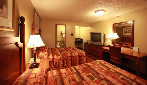 A hotel room with two beds, a desk, a television, and a mirror.