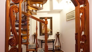 A wooden spiral staircase with ornate railings and patterned carpet, leading to a landing area with a table and chairs.