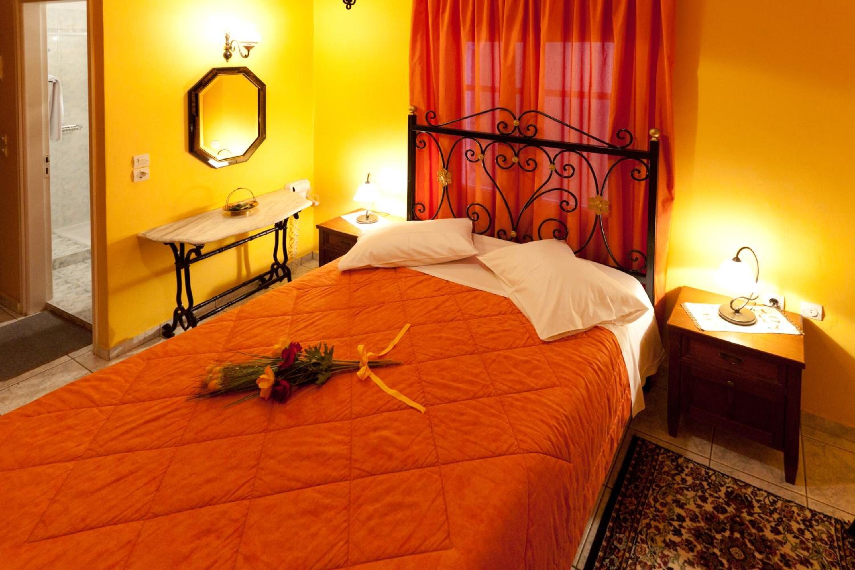 A hotel room with a bed, a bedside table, a nightstand, a mirror, and a window with curtains.
