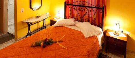 A hotel room with a bed, a bedside table, a nightstand, a mirror, and a window with curtains.