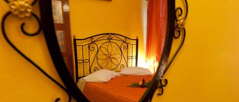 A bed with a white pillow and orange bedspread, a wooden headboard, and a mirror on the wall.