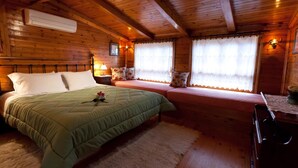 A wooden cabin bedroom with a bed, a sofa, a fireplace, and a window with curtains.