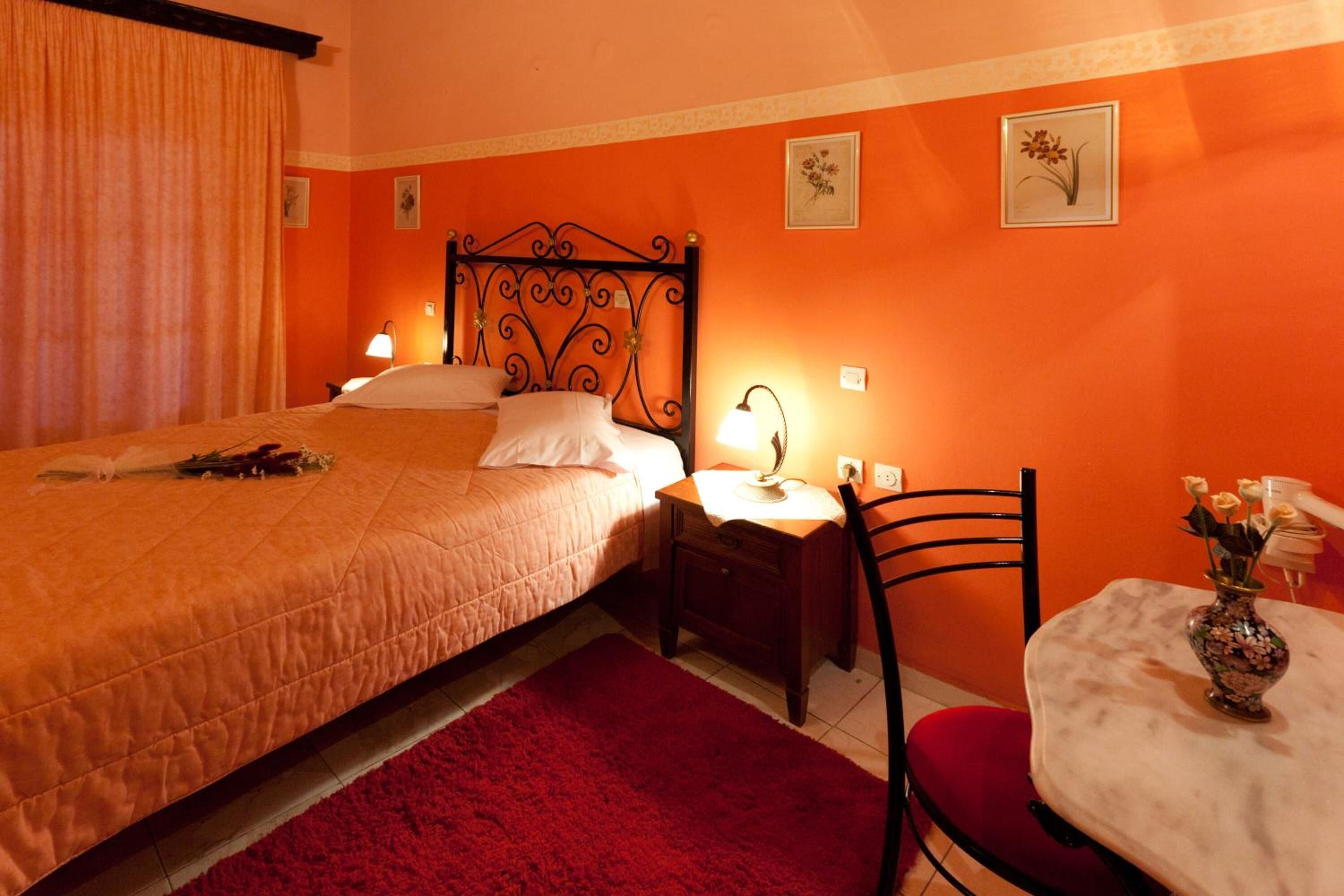 A room with a bed, a nightstand, a chair, and a small table with a vase of flowers.
