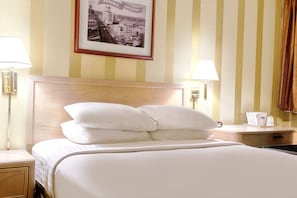 A hotel room with a large bed, two bedside lamps, a nightstand, a framed cityscape picture on the wall, and a window with curtains. - Travelodge by Wyndham Phoenix Downtown (Phoenix)