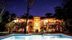 Un grand bâtiment illuminé, avec une piscine devant.