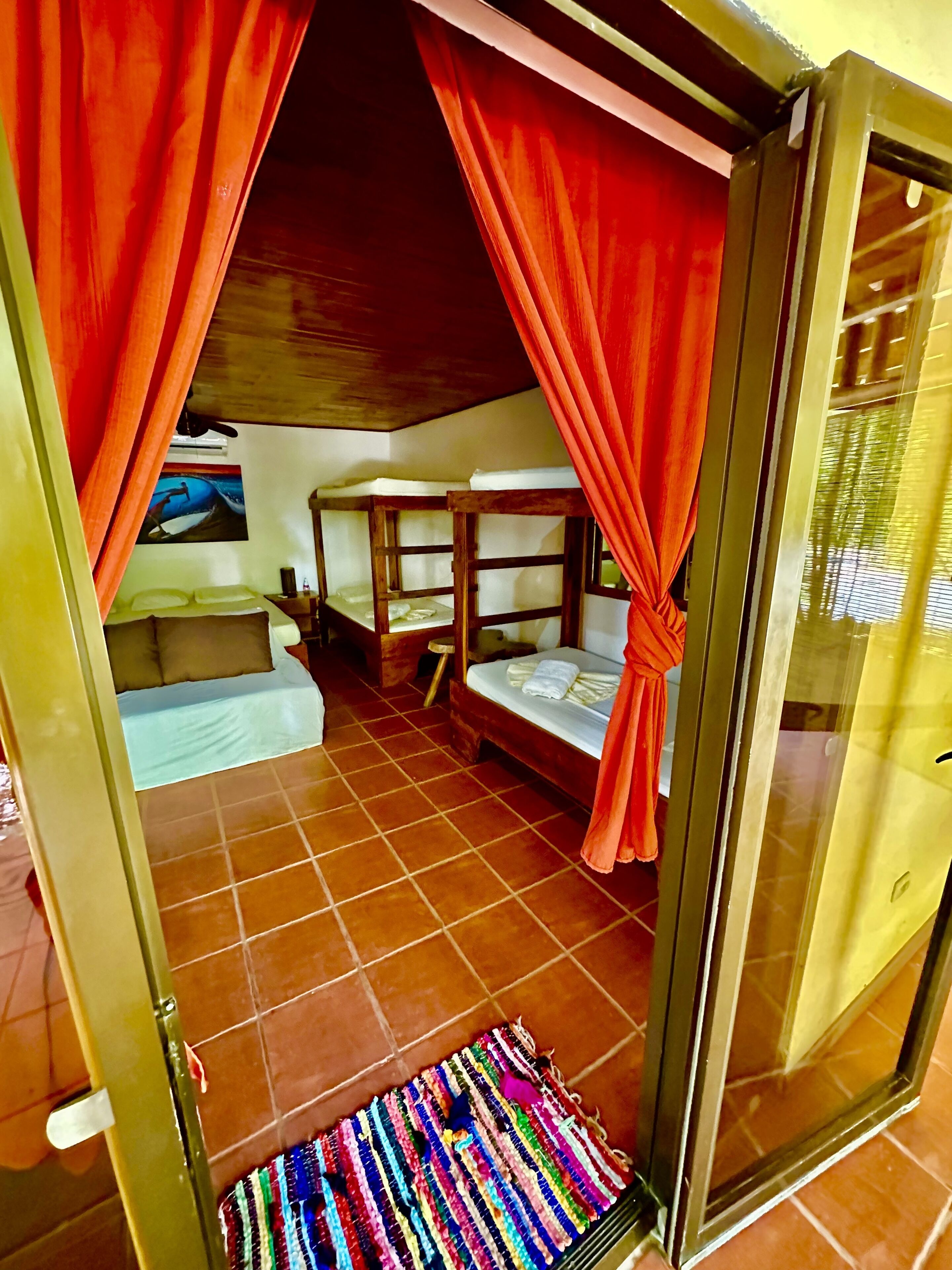 A room with a bed, a small table, and a bench. There is a window with curtains.