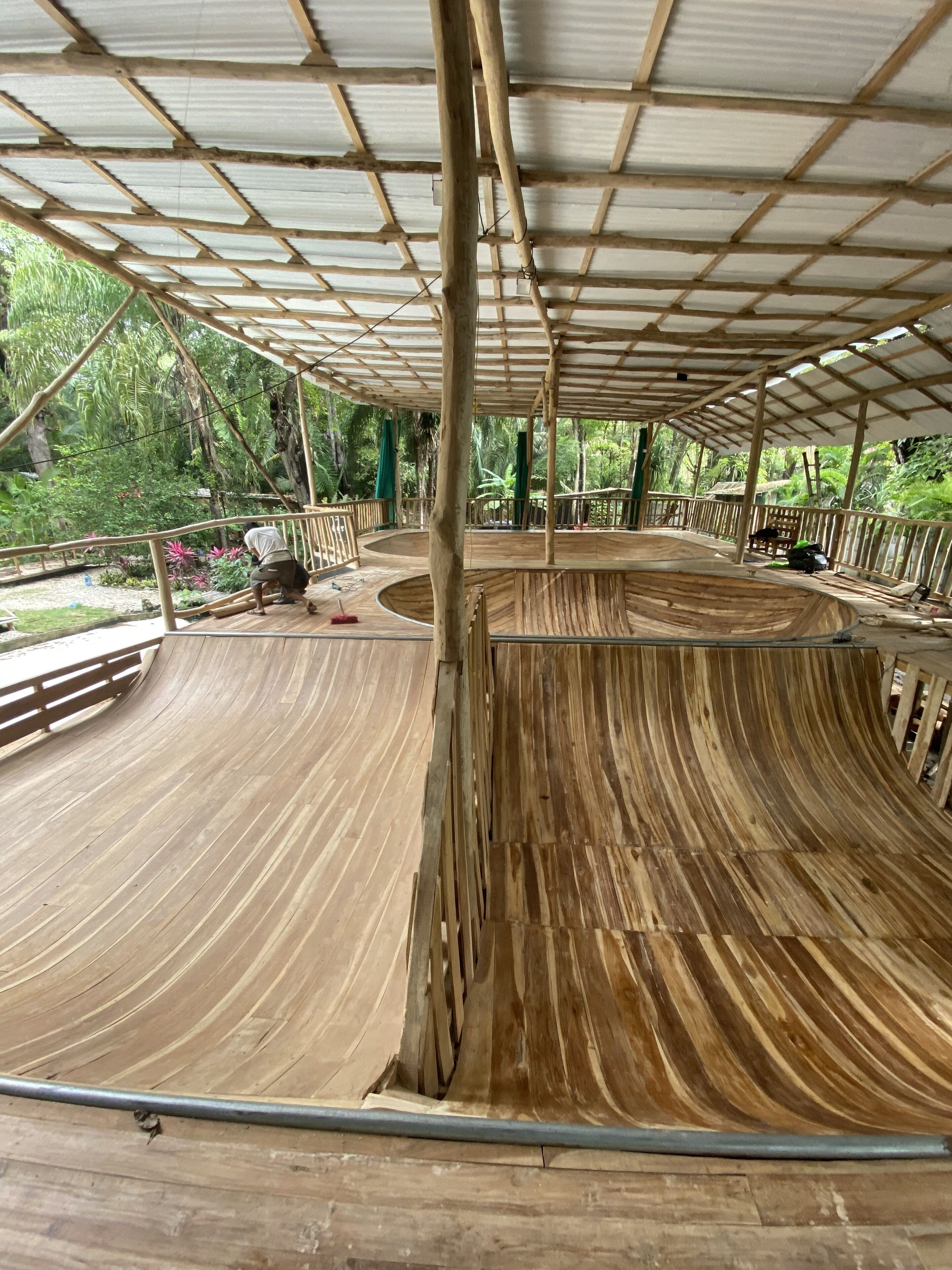 Ein Skatepark aus Holz mit einer gebogenen Rampe und einem überdachten Bereich mit Metalldach.